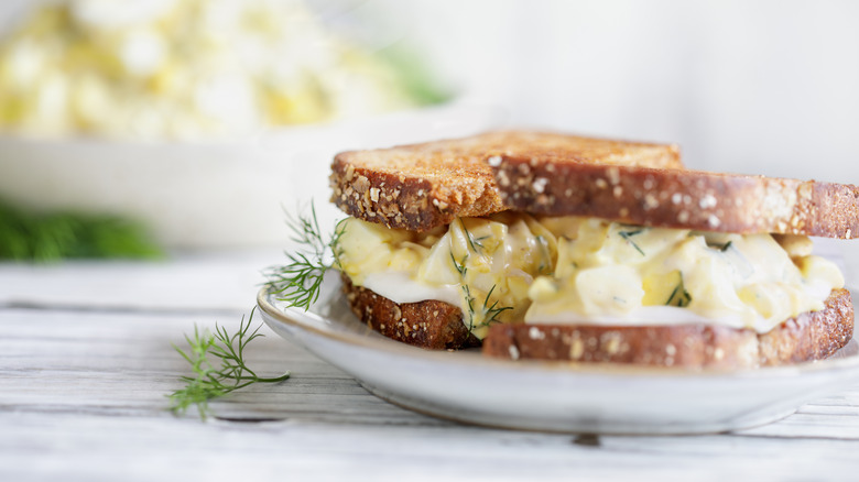 Egg salad sandwich on plate with dill garnish