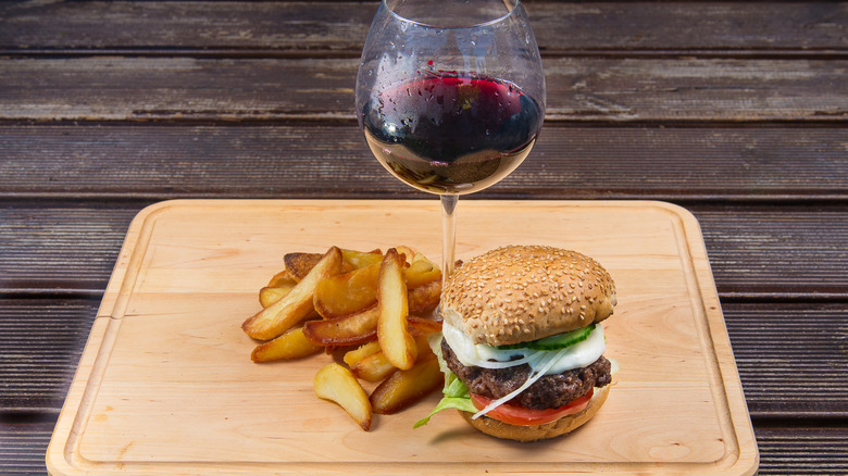 Burger and fries with a glass of red wine on a wooden board