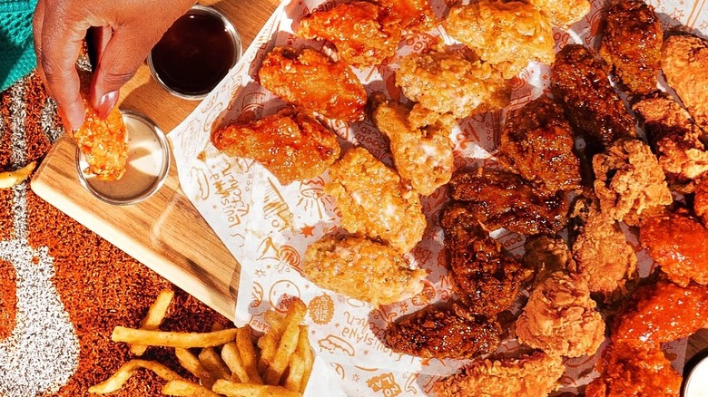 A platter of different Popeyes wings sits on a table with sides of fries, dips, mac and cheese, and more