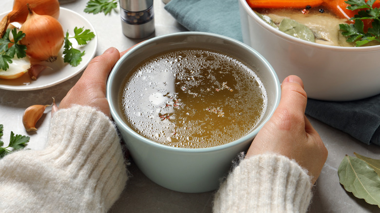 A woman holds onto either side of a bowl of warm stock