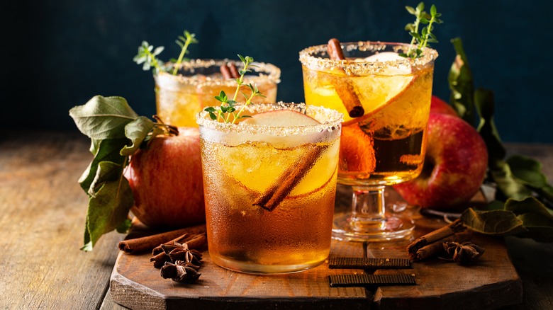 cocktails with sugar rims, apple slices, cinnamon sticks on a wooden board with whole apples