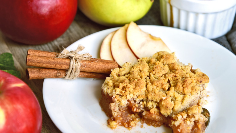 Apple cobbler served on a plate alongside apple and cinammon.