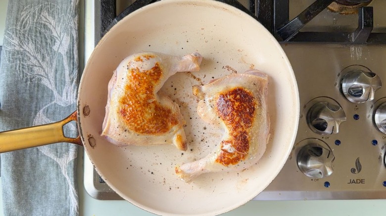 Chicken leg quarters browning in large white skillet on stovetop