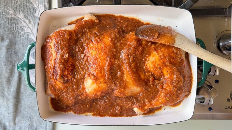 Brushing applesauce barbecue sauce onto chicken leg quarters in baking dish
