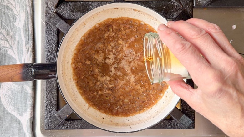 Pouring bourbon into shallots in brown butter in saucepan on stovetop