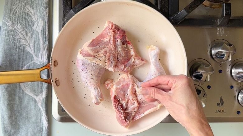 Seasoning chicken leg quarters in large white skillet