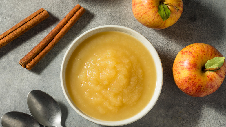 Applesauce in a bowl, cinnamon sticks, and whole apples