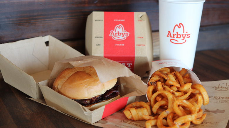 An Arby's sandwich with a drink and curly fries.