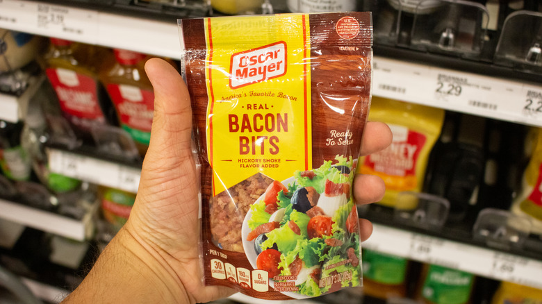 A hand holds a bag of Oscar Mayer real bacon bits