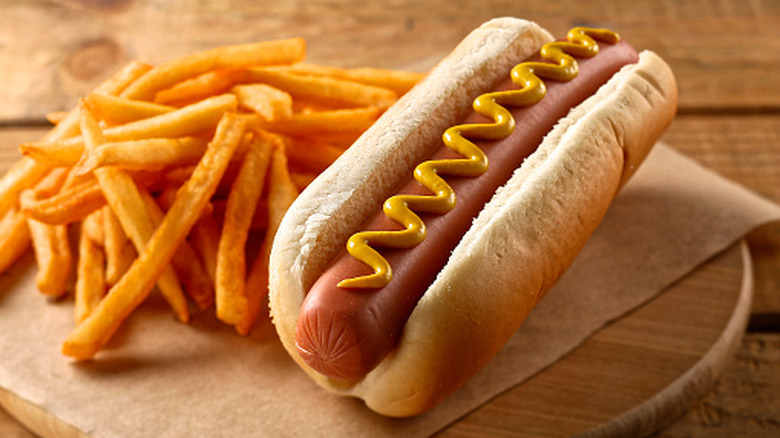 A hot dog in a bun with mustard sits on parchment paper next to french fries
