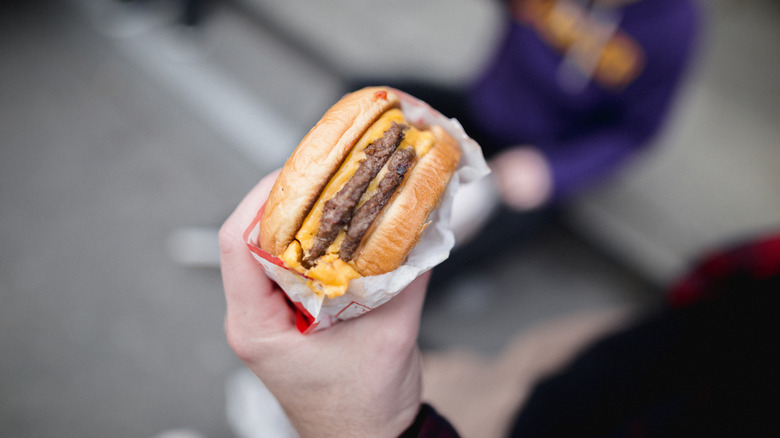 A hand holds a double cheeseburger wrapped in parchment paper