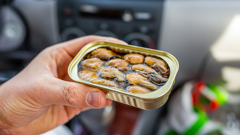 A person holds an open tin of whole oysters