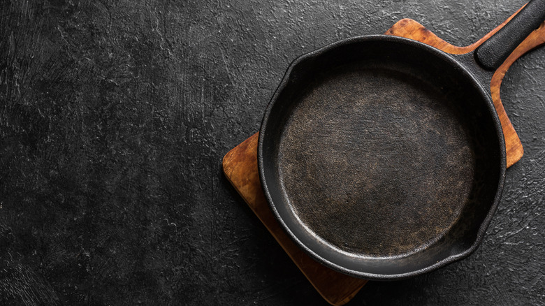 A cast iron skillet sits on a wooden board against a dark background