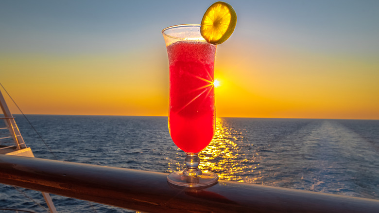 Topical red beverage balancing on cruise ship handrail at sunset
