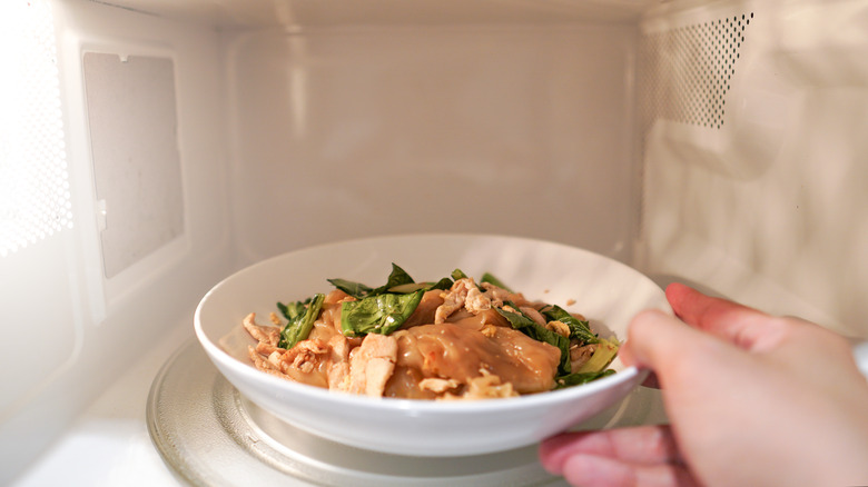 A hand places a white bowl of food inside a microwave
