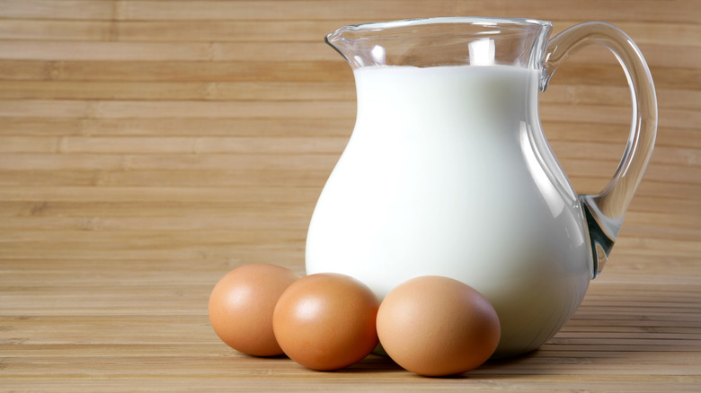 Three brown eggs next to a pitcher of milk