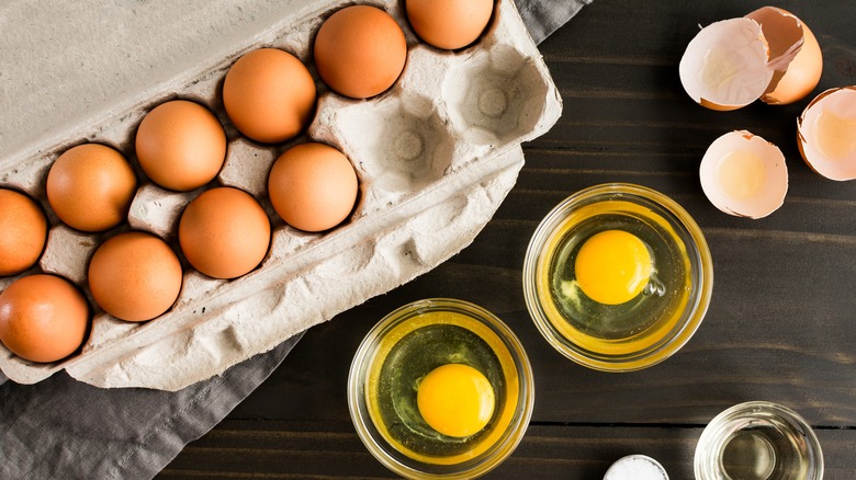 Dishes with cracked eggs next to a paper egg carton and broken brown egg shells