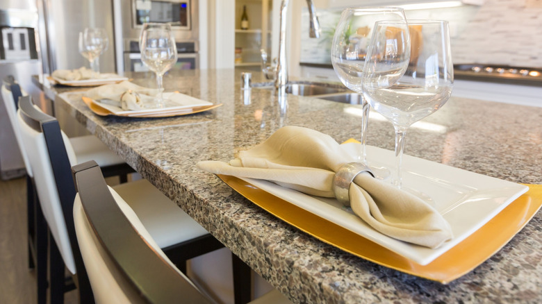 Place settings, including plates, goblets, and napkins with rings, sit on a granite kitchen island