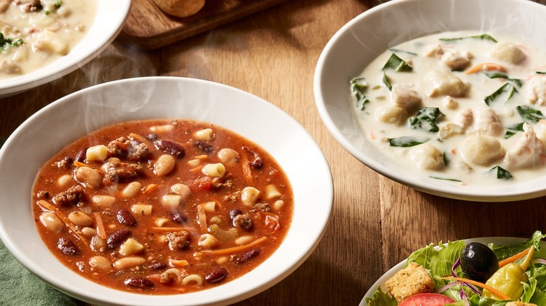Several bowls of Olive Garden soup options on a wooden table