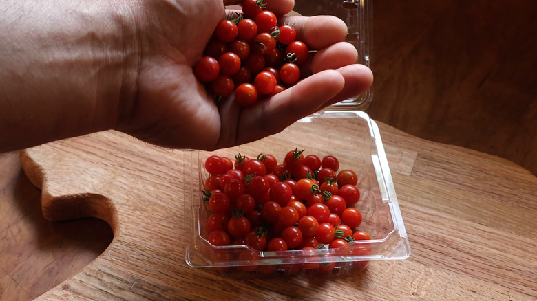 Someone holds a handful of spoon tomatoes above a container of the tiny berry-like tomatoes.