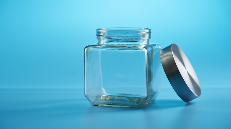 An empty glass jar, with its lid propped up next to it, sits against a blue background