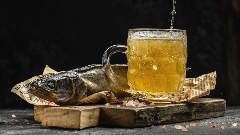Beer poured into large glass with dried fish wrapped in newspaper