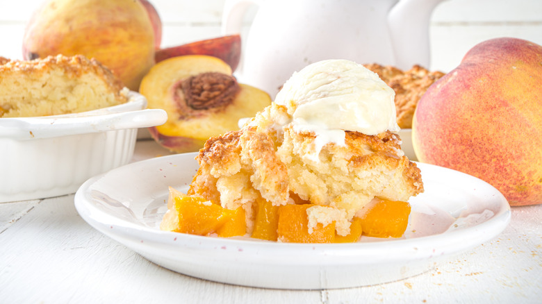 Piece of peach cobbler topped by vanilla ice cream on a plate