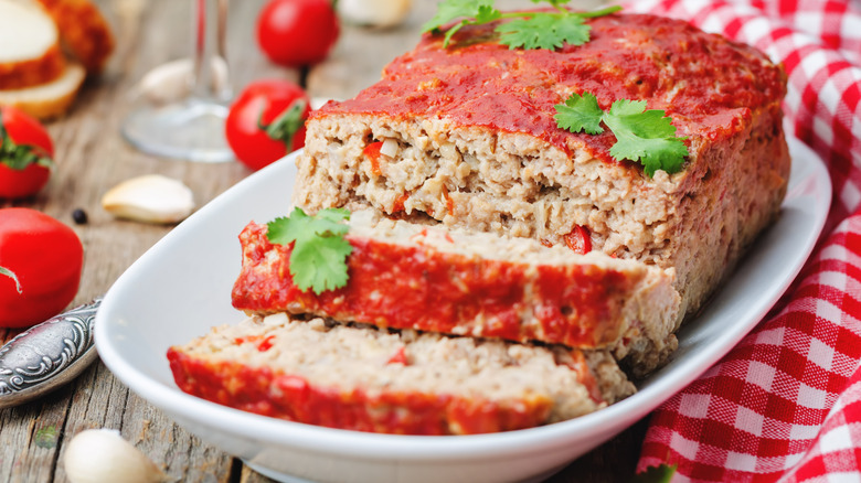 Partially sliced meatloaf in a white serving dish
