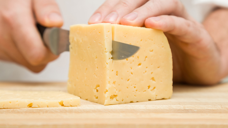 Hands cutting a cheese on the wooden board
