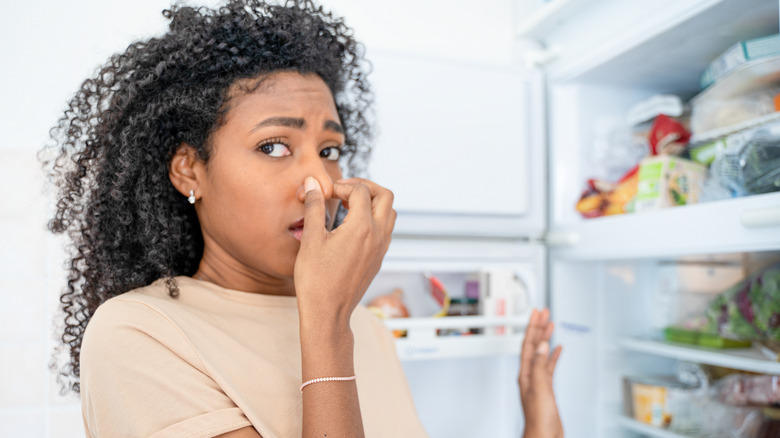 Woman smelling stinky and dirty fridge