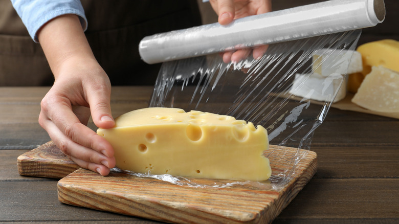 Woman putting plastic food wrap over block of cheese