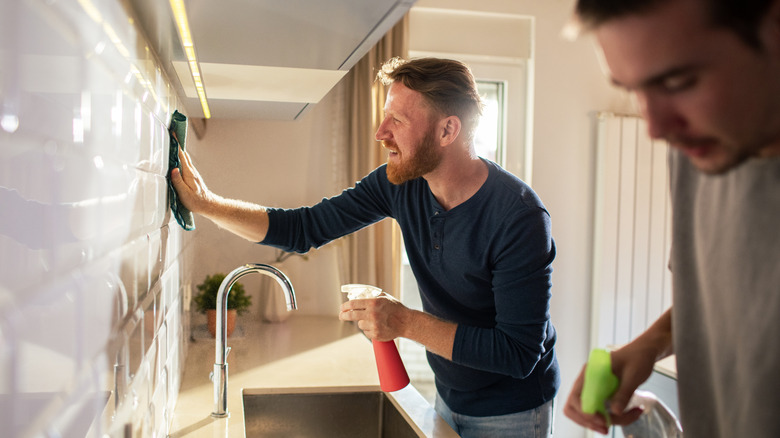 Two home owners cleaning a kitchen wall with spray bottle and rag