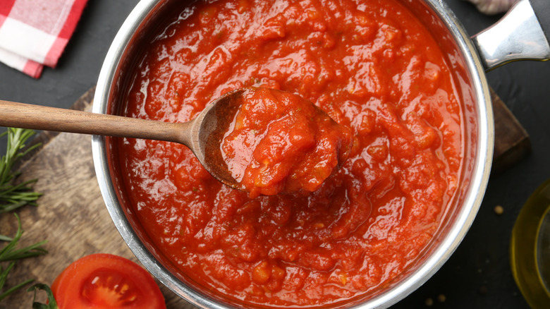 Wooden spoon scooping marinara sauce from a pan