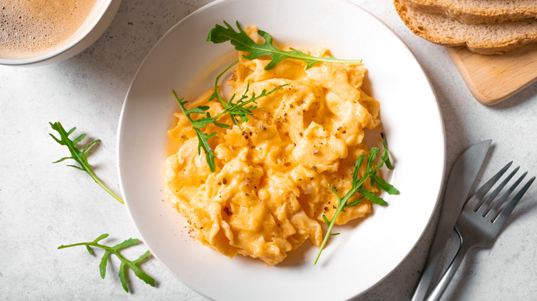 Scrambled eggs are on a white plate next to coffee and toast.