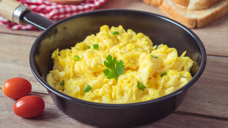 Scrambled eggs in a pan on a wooden table.