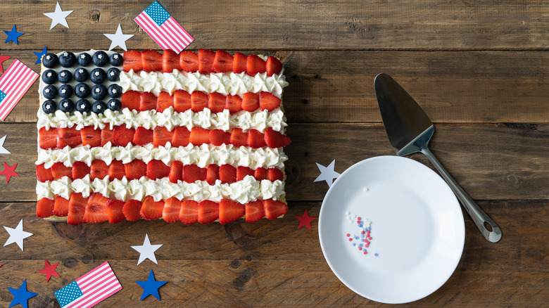 A flag cake with American flags and paper stars next to a plate and spatula