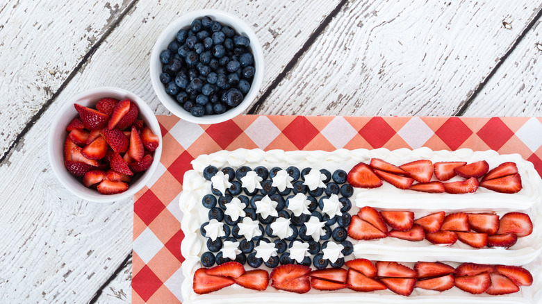 A flag cake with bowls of strawberries and blueberries on the side