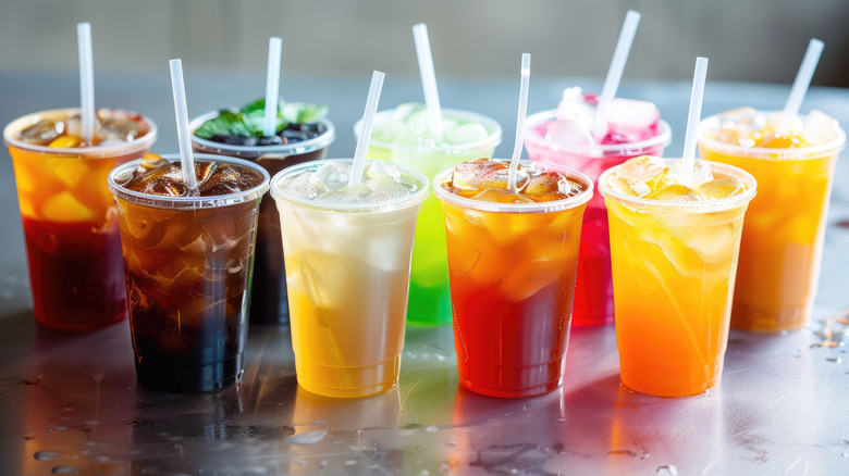 An assortment of beverages lined up, all in plastic cups with ice and straws.