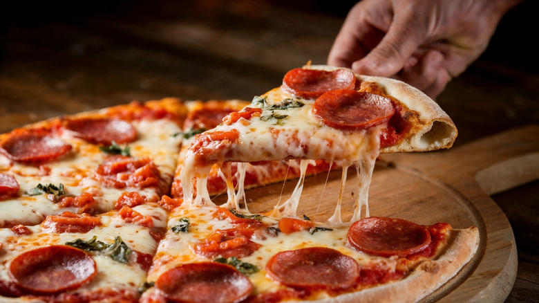 Cooked pepperoni pizza slice being taken from the pie