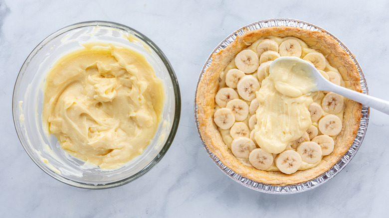 Pie crust with sliced bananas inside and vanilla pudding being spooned in from a bowl