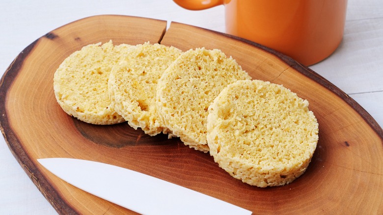 Round slices of bread on board next to knife and mug