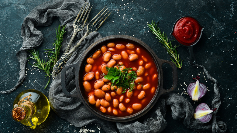 pot of beans surrounded by herbs, oil, aromatics, and two forks 