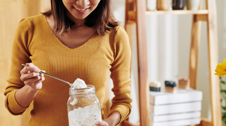 person taking a spoonful of baking soda out of a jar