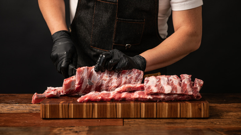 A butcher preparing raw pork ribs on a cutting board