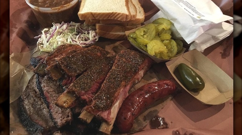 A plate of ribs, brisket, slaw, beans, bread, and veggies on butcher paper at Franklin Barbecue