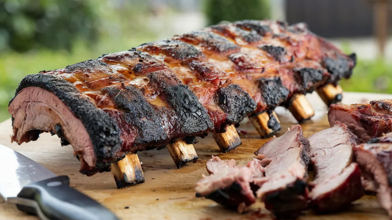A rack of grilled beef ribs rest on an outdoor wooden table