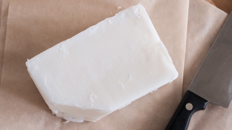A slab of beef tallow on parchment paper next to a knife
