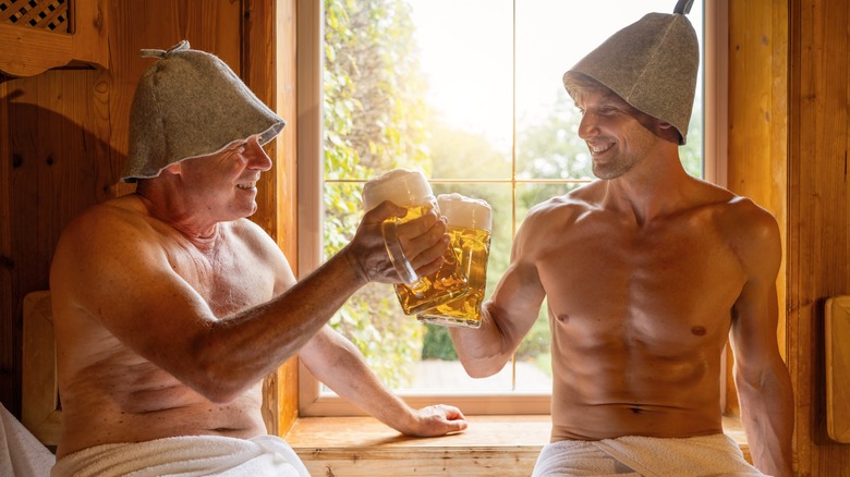 Topless older man and younger man toasting with large beer mugs in a beer spa sauna