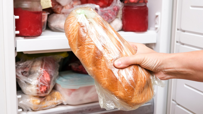 A hand holds onto a loaf of bread before putting it in the open freezer