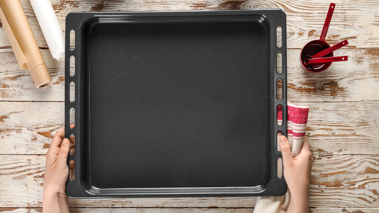 A person holding a baking tray in front of a wooden table